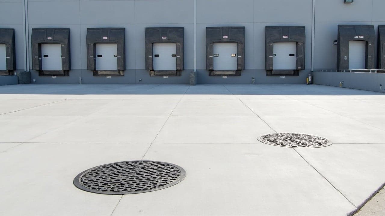 Cour en béton d'un bâtiment logistique récent avec deux tampons en fonte affleurants devant les quais de chargement